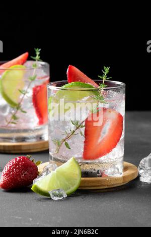 Cocktail mojito con fragole fresche. Due bicchieri con soda estiva fredda alla fragola con fragola, cubetti di ghiaccio e lime, decorata con timo scuro Foto Stock