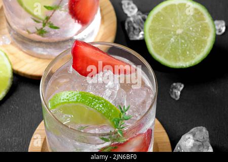 Cocktail mojito con fragole fresche. Due bicchieri con soda estiva fredda di fragola con fragola, ghiaccio e lime, decorata con timo su sfondo scuro Foto Stock