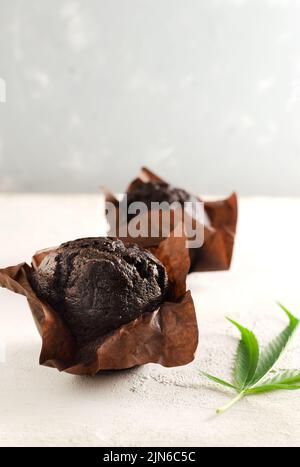 Muffin al cioccolato marroni con cannabis. Dolci alternativi. Muffin marijuana con foglie di cannabis. Senza glutine. Orientamento verticale. S Foto Stock