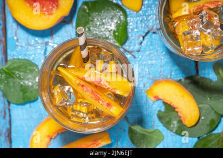 Tè fatto in casa al ghiaccio di pesca con pesche fresche mature su sfondo blu di legno di alto colore Foto Stock