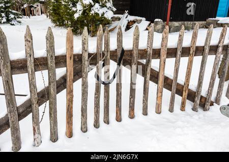 Vecchia recinzione in legno protetta da serratura numerica. Clima invernale innevato. Scarsa protezione dell'edificio. Foto Stock