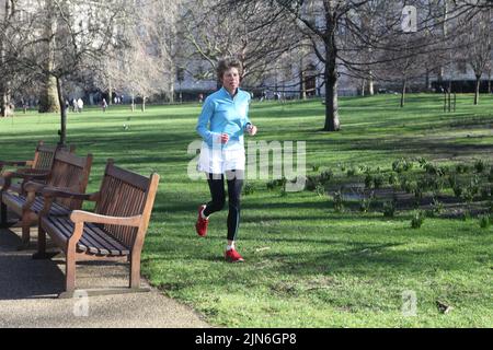 Entusiasta jogger femminile sta facendo la sua strada da banchi di legno su terreno più morbido di asfalto pavimentazione erba il giorno soleggiato di febbraio a St James Park Londra Foto Stock