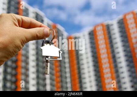 Agente immobiliare, portachiavi a forma di casa e chiave in mano maschile sullo sfondo di nuovi edifici. Byung appartamento o affitto di proprietà Foto Stock