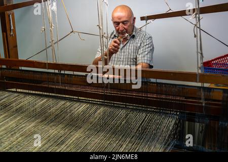Ardara, Irlanda - 13 luglio 2022: Maestro artigiano che lavora su un tradizionale telaio in legno e tessitura a mano di lana di tessuto a spina di pesce Foto Stock