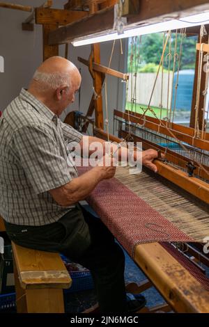 Ardara, Irlanda - 13 luglio 2022: Maestro artigiano che lavora su un tradizionale telaio in legno e tessitura a mano di lana di tessuto a spina di pesce Foto Stock