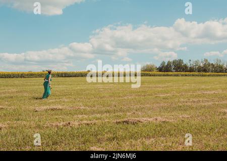 Donna in verde passeggiate attraverso estate campo soleggiato Foto Stock