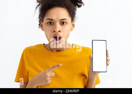 giovane donna sorpresa con telefono cellulare su sfondo bianco guardando la fotocamera Foto Stock