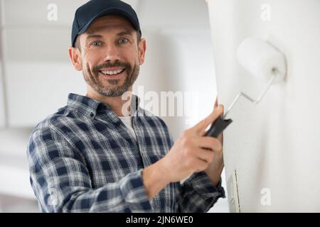 uomo pittore in vetri dipinge le pareti con un rullo Foto Stock