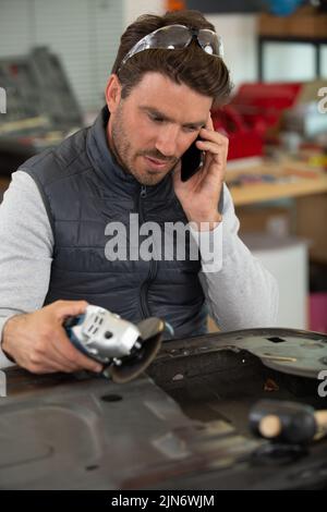 operatore che utilizza una smerigliatrice angolare su una porta dell'auto Foto Stock