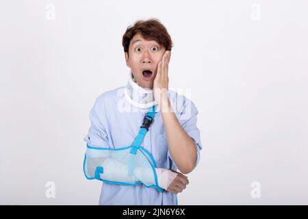 Ritratto di uomo asiatico con braccio rotto e collo sensazione di sorpresa e scioccato isolato su sfondo bianco copia spazio Foto Stock