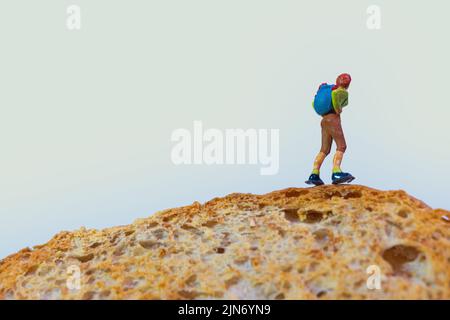 un escursionista con uno zaino si trova sopra una fetta di pane tostato, primo piano, foto macro, sfondo bianco Foto Stock