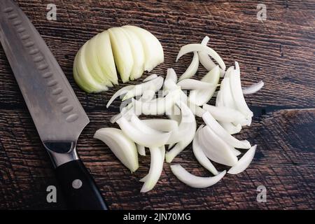 Cipolla tagliata a fette sottili su un tagliere di legno scuro: Cipolla tagliata a fette sottili con un coltello dello chef su un fondo di legno Foto Stock