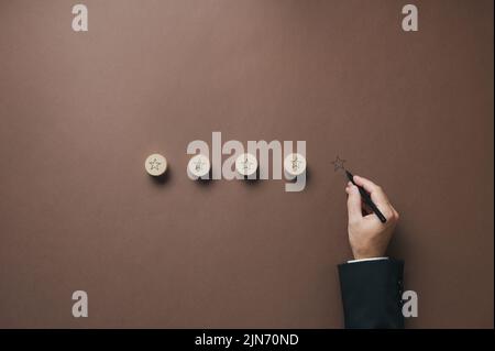 Quattro stelle disegnate su cerchi di legno tagliati con una mano di un uomo d'affari che disegnano la quinta sul backgorund marrone in un'immagine concettuale di eccellenza Foto Stock