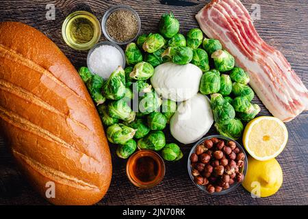 Brussels Sprout toast caramellato con Burrata & Bacon ingredienti: Pane fresco, germogli di Bruxelles e altri ingredienti su sfondo di legno Foto Stock