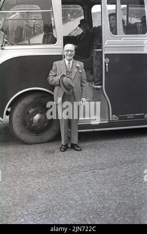 1950s, storico, viaggio in pullman, un Signore anziano, vestito con un abito in tre pezzi, giacca, gilet & cravatta, fiore in lapel e cappello in mano, in piedi fuori dalla porta d'ingresso del pullman, Grimesthorpe Rd, Sheffield, South Yorkshire, Inghilterra, REGNO UNITO. Sulla sua tuta, un distintivo con la parola, Segretario. Foto Stock