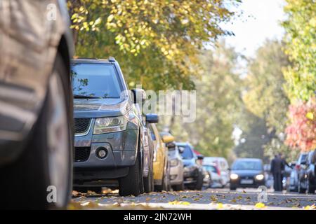 Traffico cittadino con molte auto parcheggiate in linea sul lato della strada Foto Stock