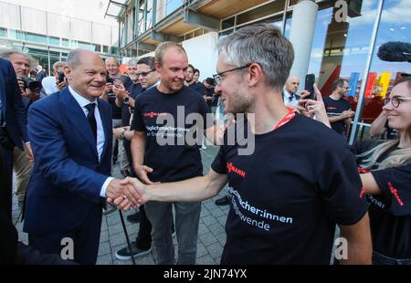 09 agosto 2022, Hessen, Allendorf (Eder): I dipendenti di Viessmann danno il benvenuto al cancelliere tedesco OLAF Scholz (SPD - l) nella sede della società a conduzione familiare Hessian. Scholz ha appreso informazioni sulle pompe di calore e sulle soluzioni per il clima verde presso l'azienda Viessmann. Foto: Nadine Weigel/dpa Foto Stock