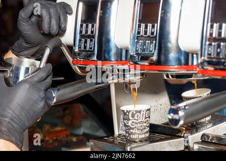 Le mani del barista in guanti in lattice nero preparano il caffè caldo in una macchina da caffè. Foto Stock