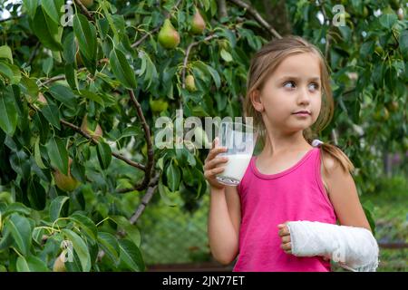 Ragazza piccola carina con un braccio rotto in un cast bere latte e godere. Riabilitazione dopo una frattura Foto Stock