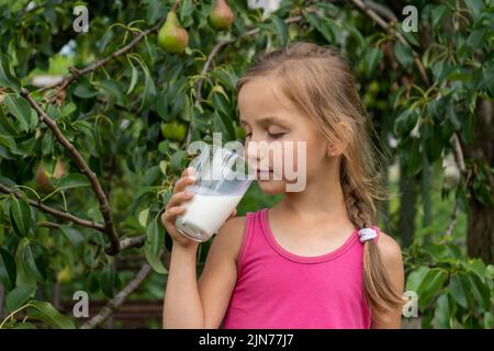 Bella bambina beve latte. Albero con pere sullo sfondo Foto Stock