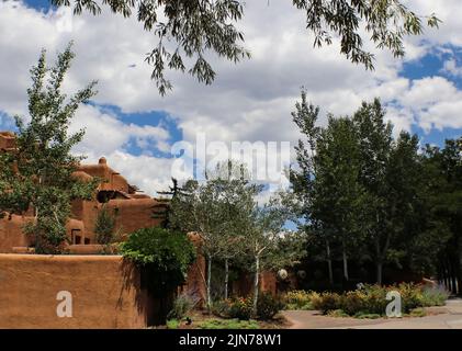 Architettura di adobe sud-occidentale sotto un cielo blu con le nuvole bianche e soffice circondato e incorniciato da alberi Foto Stock