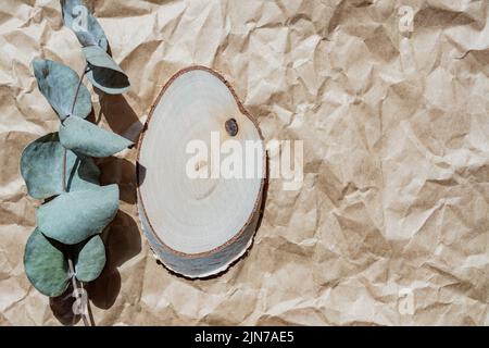 Podio rotondo vuoto in legno per la presentazione del prodotto, ramo di eucalipto su sfondo artigianale di carta. Sfondo di materiali naturali per pubblicità cosmetica Foto Stock