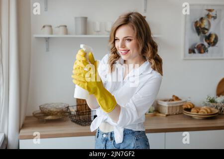 Una ragazza in guanti gialli tiene uno spray detergente sullo sfondo della cucina Foto Stock