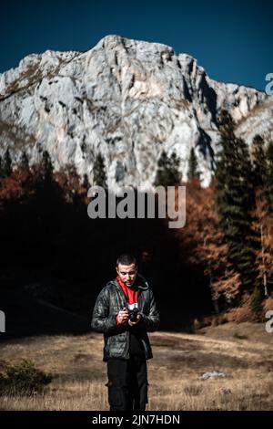 Foto verticale di una fotografia ispanica in piedi in un parco con uno sfondo sfocato di montagne rocciose Foto Stock