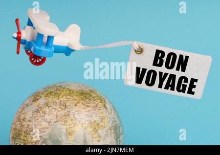 Concetto di viaggio e business. Su sfondo blu, un globo e un aeroplano con un cartello - Bon voyage. Globo fuori fuoco. Foto Stock