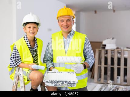 Sorridente ragazzo e padre che tiene rulli di vernice, lavori di miglioramento domestico Foto Stock