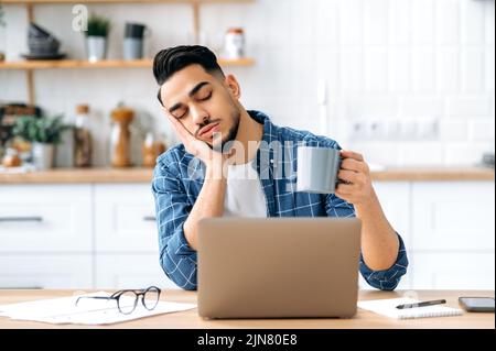 Stanco ha sovraccaricato l'uomo arabo o indiano, studente, ceo aziendale, lavorando da remoto a casa utilizzando il laptop, si è addormentato mentre lavora, stanco di noioso progetto, cronica deprivazione del sonno, chiuso gli occhi Foto Stock