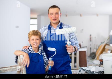 Ritratto di ragazzo e padre positivi con rulli di vernice Foto Stock