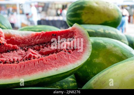 Cocomero allungato fresco con un taglio trasversale che mostra un interno rosa chunky con un sacco di semi neri e striato verde e giallo buccia esterna Foto Stock