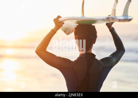 Shes colpendo l'acqua che corre. Ripresa di una surfista che porta la sua tavola da surf sulla testa in spiaggia. Foto Stock