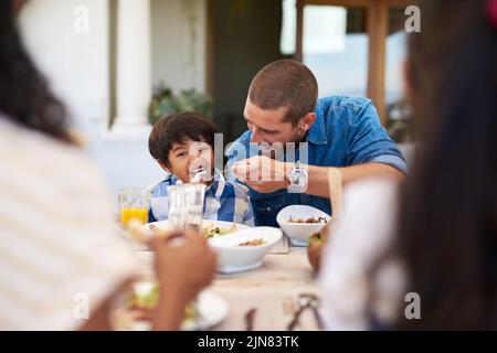 Il suo appetito cresce di giorno in giorno: Un padre che alleva il suo figlio durante un pasto con la famiglia all'aperto. Foto Stock