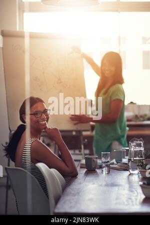 Una donna che si presenta su una lavagna per spiegare idee e pensieri durante un incontro in una sala riunioni con i colleghi. Ritratto di diverse squadre Foto Stock