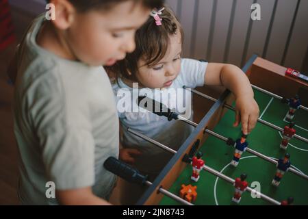 Una bambina e un ragazzo esaminano con attenzione il calcio balilla. Per un design di stile di vita. I bambini giocano con i giochi da tavolo. Buona famiglia. Foto Stock