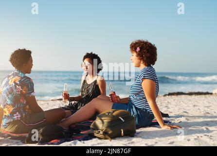 Niente batte una giornata di sole con gli amici sulla spiaggia. Foto retroguidata di un attraente giovane trio di donne che hanno un picnic sulla spiaggia durante il giorno. Foto Stock