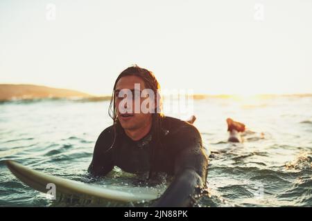 Cavalca con la marea. Un giovane uomo che si addita su una tavola da surf in mare. Foto Stock