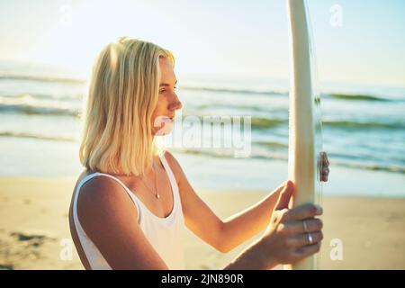 Il surf è uno stile di vita. Una giovane donna attraente in piedi in un costume da bagno che tiene una tavola da surf sulla spiaggia. Foto Stock
