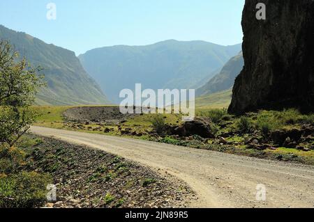 Svolta a sinistra su una strada di ghiaia che corre lungo il fondo di un profondo canyon circondato da alte montagne. Valle del fiume Chulyshman, Altai, Siberia, Russia. Foto Stock