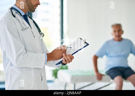 Il benessere dei suoi pazienti è la sua passione, un giovane medico irriconoscibile che compila un archivio con il paziente anziano in background. Foto Stock