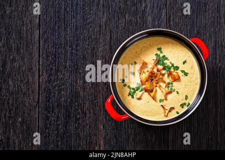 Kanttarellikitto, zuppa finlandese di Chanterelle in pentola rossa su tavolo di legno scuro, vista orizzontale dall'alto, giacitura piatta, spazio libero Foto Stock