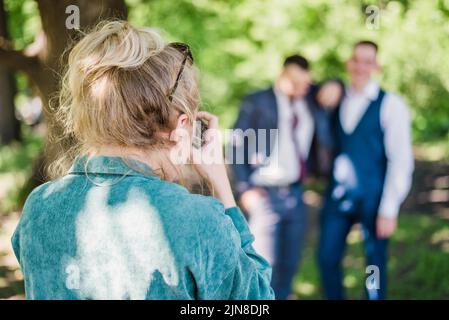 Un fotografo di nozze scatta foto degli ospiti della sposa e dello sposo in natura in una giornata di sole Foto Stock