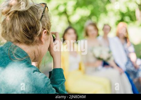 Un fotografo di nozze scatta foto degli ospiti della sposa e dello sposo in natura in una giornata di sole Foto Stock