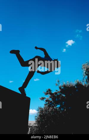 La silhouette nera di un uomo irriconoscibile che pratica il parkour. Uomo con il cielo sullo sfondo che fa un somersault. L'uomo in aria nel mezzo di un Foto Stock