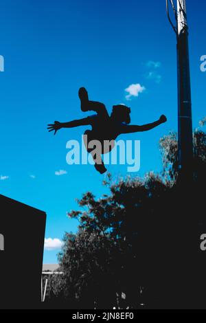 La silhouette nera di un uomo al centro di una ruota. Parkour atleta pratica. La silhouette scura di un giro nell'aria di un acrobata. Irriconoscibile Foto Stock