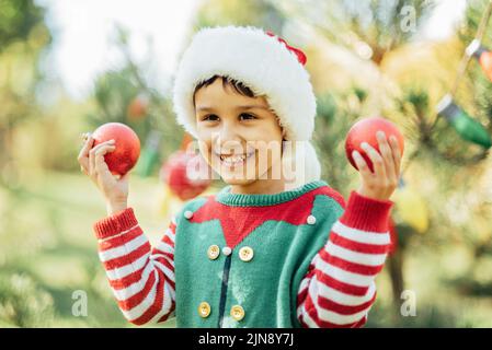 Natale nel mese di luglio. Bambino in attesa di Natale in legno in estate. Ritratto di ragazzo decorazione albero di natale. Vacanze invernali e concetto di persone. Buon Natale e buone feste Foto Stock