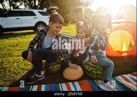 Quattro bambini che trascorrono il tempo insieme. Coperta per picnic all'aperto, seduta con cocomeri. Foto Stock