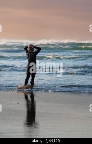 Un uomo che indossa un costume da bagno in piedi da solo sulla costa di Crantock Beach a Newquay in Cornovaglia. Foto Stock